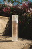 Skincare bottle labeled 'Arugot' on a stone surface with flowers in the background