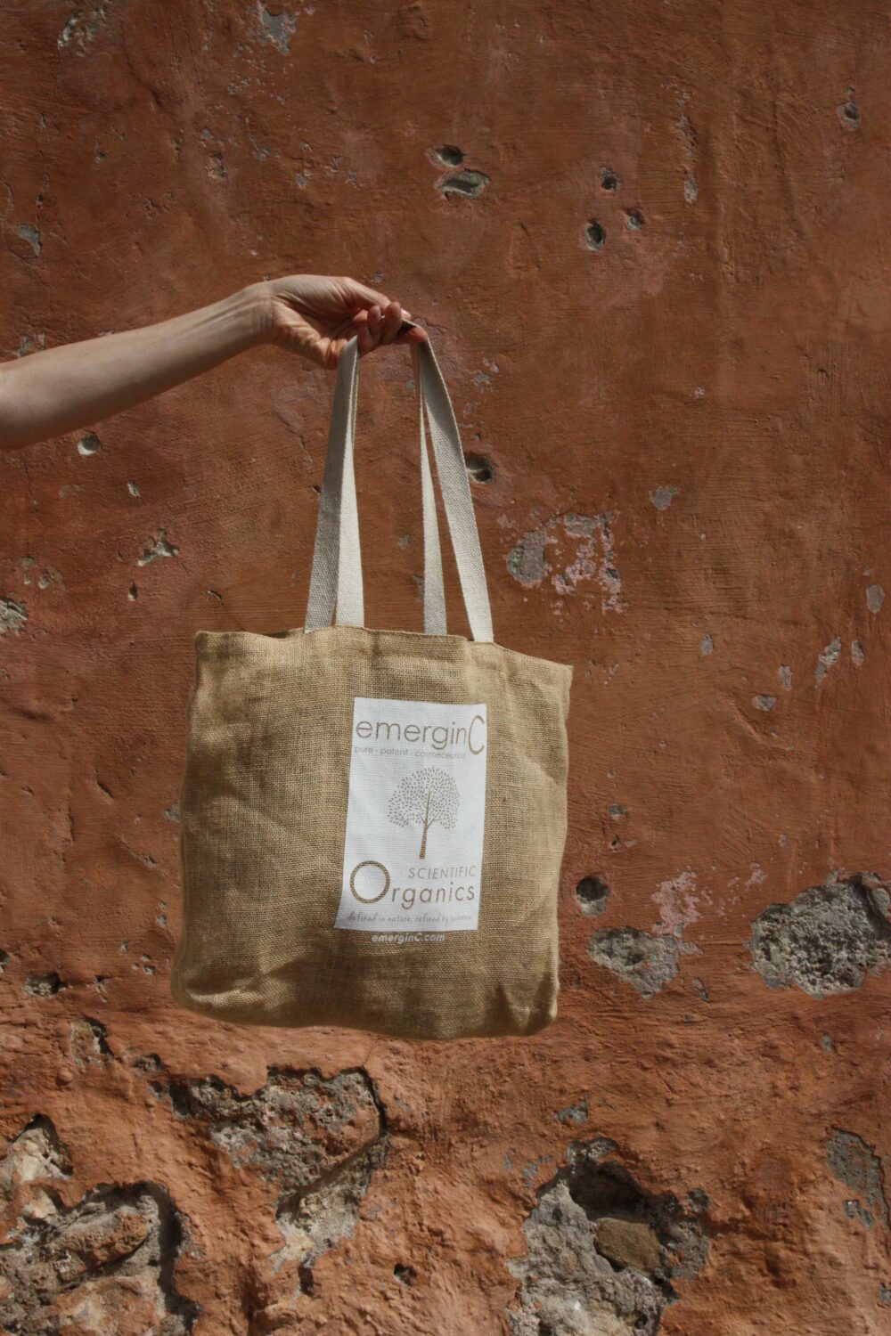emerginC burlap bag from Scientific Organics line held against reddish-brown wall