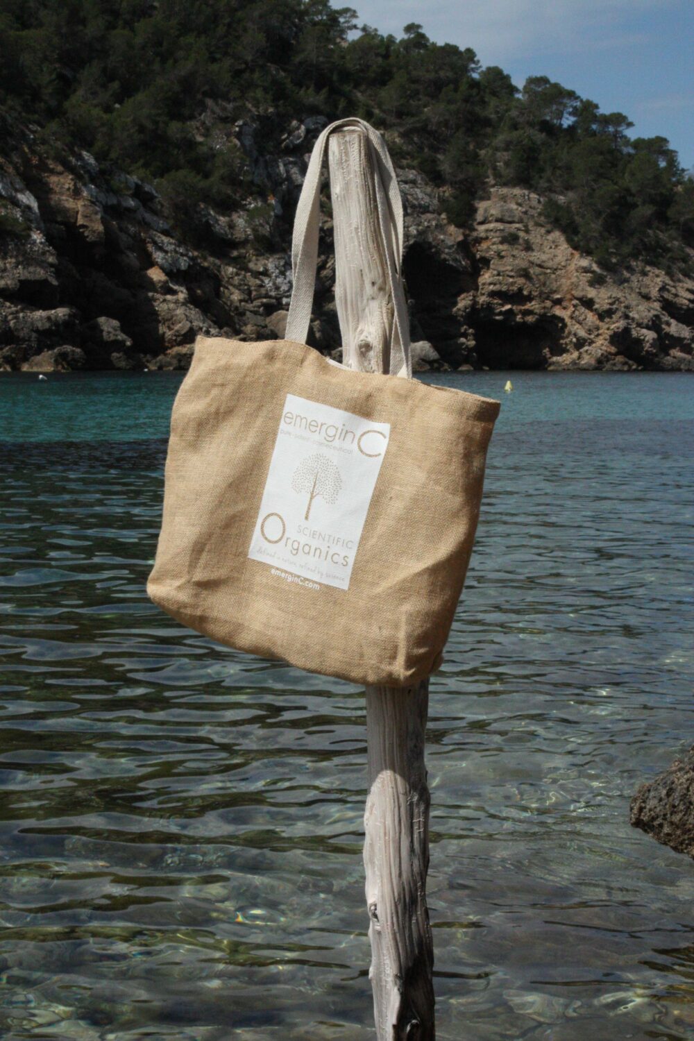 emerginC Scientific Organics bag hangs from wooden pole in beautiful bay in Ibiza